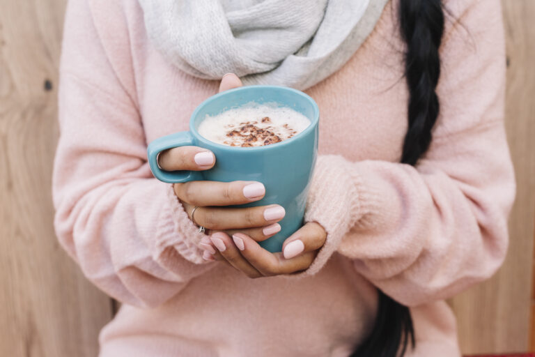 A person wearing a pink sweater and pink nails hold a hot chocolate mug.